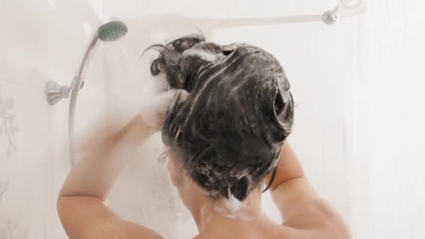 Naga kobieta bierze prysznic. Kobieta myje krótkie włosy szamponem. Film w zwolnionym tempie w białej łazience. — Wideo stockowe
