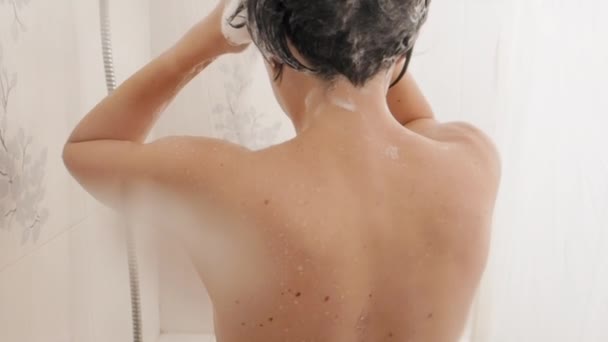 Una mujer desnuda toma una ducha. La mujer se lava el pelo corto con champú. Vídeo en cámara lenta en baño blanco . — Vídeos de Stock