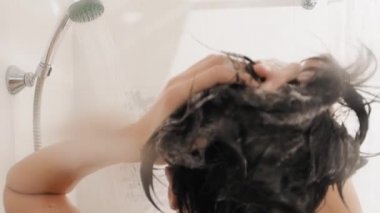 Naked woman takes a shower. Woman washes her short hair with shampoo. Slow motion video in white bathroom.