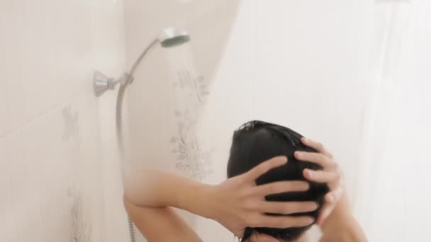 Meztelen nő zuhanyozik. A nő samponnal mossa a rövid haját. Lassított mozgású videó fehér fürdőszobában. — Stock videók