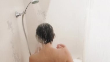 Naked woman takes a shower. Woman washes her short hair with shampoo. Slow motion video in white bathroom.