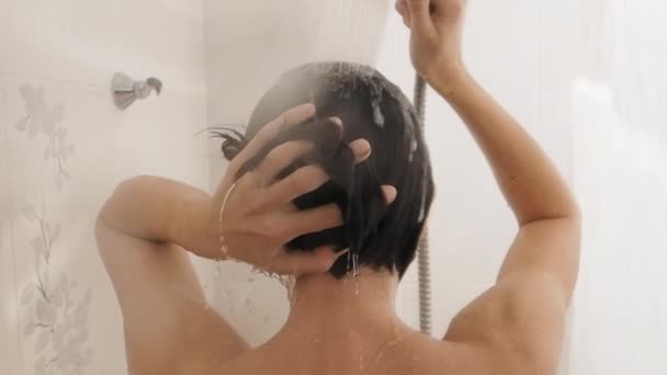 Una donna nuda si fa una doccia. Donna lava i capelli corti con lo shampoo. Video al rallentatore in bagno bianco . — Video Stock