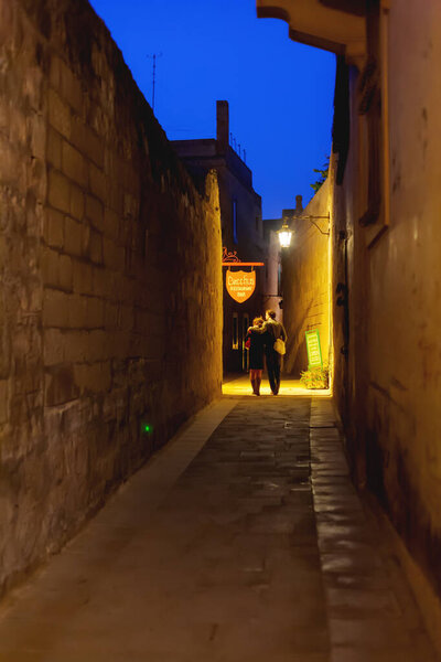 MDINA, MALTA - February 19, 2010. People walking down narrow streets with cafes and restaurants. Night view on illuminated buildings and wall decorations of ancient town.