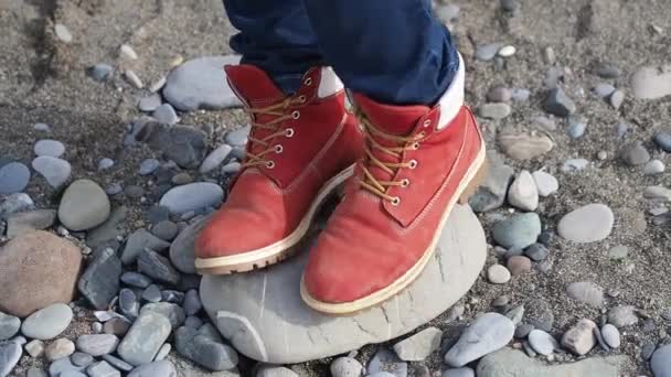 Woman in bright red boots stays on rocky beach. Hiking. — Stock Video