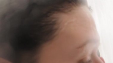 Çıplak kadın duş alıyor. Kadın kısa saçlarını suyla yıkıyor. Beyaz banyoda yavaş çekim videosu.