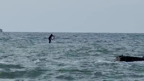 Ο άνθρωπος κωπηλατεί πάνω σε ένα SUP. Σήκω πάνω κάνοντας σερφ. Θαλάσσια σπορ στη Μαύρη Θάλασσα, Σότσι, Ρωσία. — Αρχείο Βίντεο