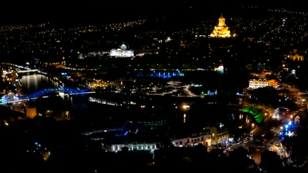 Vista panorâmica noturna da capital Tbilisi do país da Geórgia. Igreja Metekhi Catedral da Santíssima Trindade Sameba e Administração Presidencial à noite com iluminação e carros em movimento — Vídeo de Stock