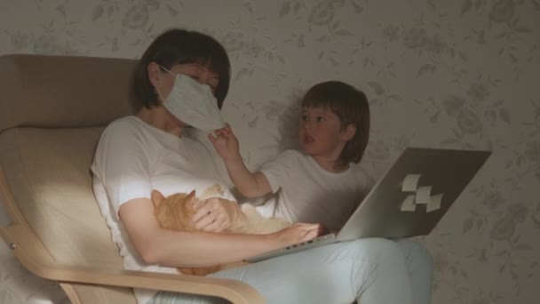 Mor, barn son och katt sitter tillsammans på stol med laptop. Kvinnan försöker arbeta på distans, men grabben ber om spel eller tecknade serier. Karantänavstängning på grund av coronavirus COVID-19. 10bit V-logL — Stockvideo