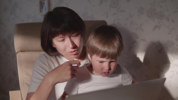 Madre y su niño pequeño se sientan juntos en la silla con el ordenador portátil. Mujer trata de trabajo remoto, pero el niño está pidiendo juego o dibujos animados. bloqueo de cuarentena por coronavirus COVID-19. V-logL de 10bit — Vídeos de Stock