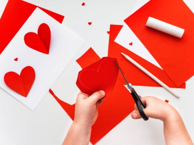 Çocuk ya Anneler Günü 'nde ya da Sevgililer Günü' nde tebrik kartı atıyor. Kırmızı kağıt hacimsel kalp ile DIY tatil kartı, aşkın sembolü. Çocuk eliyle yapılan makas, yapıştırıcı ve renkli kağıtlar. 12. adımın 4. aşaması.