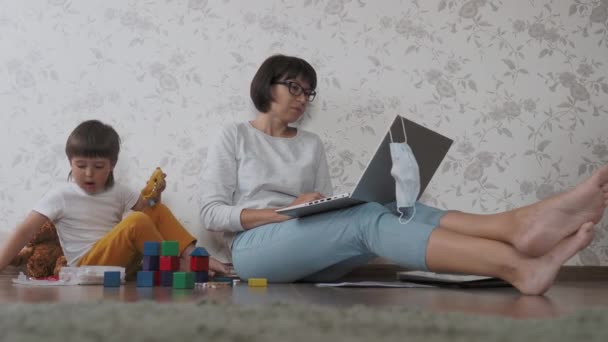 Maman et son fils se disputent à la quarantaine à la maison à cause du coronavirus COVID19. Mère télécommande fonctionne avec ordinateur portable, fils joue avec des blocs jouets. Auto-isolement à la maison . — Video