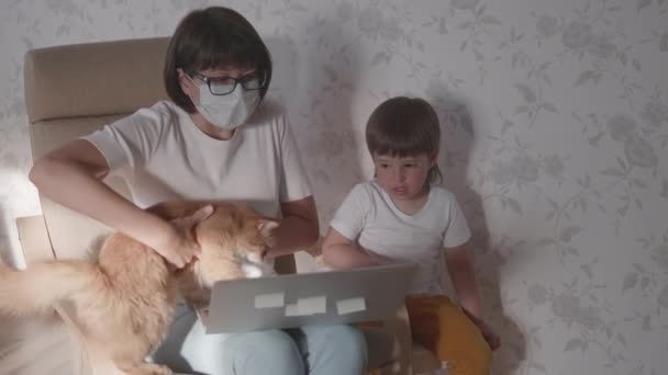 Mutter, Kleinkind und Katze sitzen zusammen auf einem Stuhl mit Laptop. Frau versucht Arbeit fernzuhalten, aber Kind fragt nach Spiel oder Cartoons. Quarantäne-Sperre wegen Coronavirus COVID-19. 10bit V-logL — Stockvideo