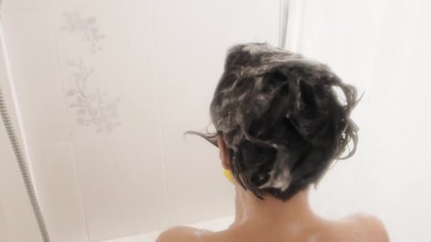 Meztelen nő zuhanyozik. A nő samponnal mossa a rövid haját. Lassított mozgású videó fehér fürdőszobában. — Stock videók