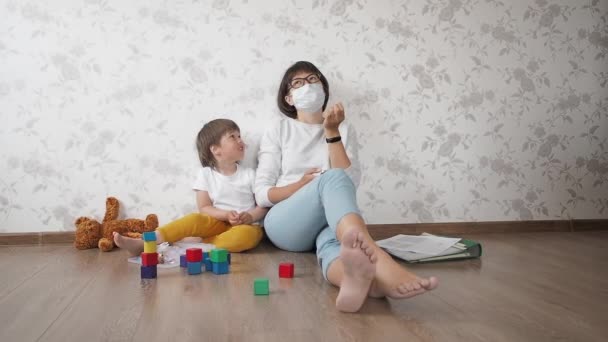 Mama i syn siedzą w domowej kwarantannie z powodu koronawirusu COVID19. Matka pracuje zdalnie z laptopem, syn bawi się klockami. Samoizolacja w domu. — Wideo stockowe