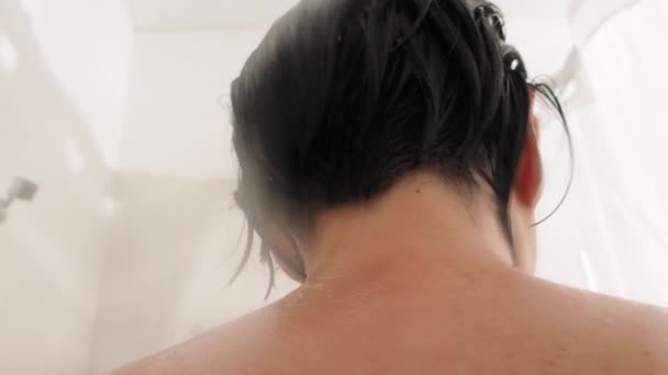 Una mujer desnuda toma una ducha. La mujer se lava el pelo corto con agua. Vídeo en cámara lenta en baño blanco . — Vídeo de stock