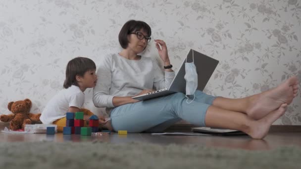 Mamma e figlio stanno in quarantena a causa del coronavirus COVID19. Il telecomando di madre lavora con computer portatile, il figlio gioca con blocchi giocattolo. Auto isolamento a casa . — Video Stock