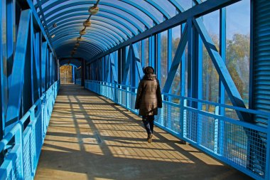 A woman walks on a overhead pedestrian bridge in the city clipart