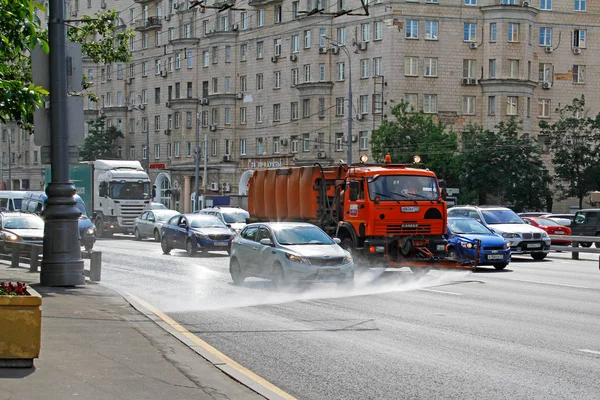 Μηχανή δρόμο flusher και οχήματα ιππασίας στο δρόμο της πόλης. Πότισμα μηχανή πλένει την οδική σκόνη και βρωμιά — Φωτογραφία Αρχείου