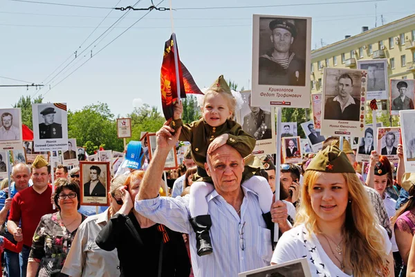 Una chica en uniforme militar con bandera se sienta sobre los hombros de su abuelo en la acción "Regimiento inmortal" en el día de la victoria en Volgogrado —  Fotos de Stock
