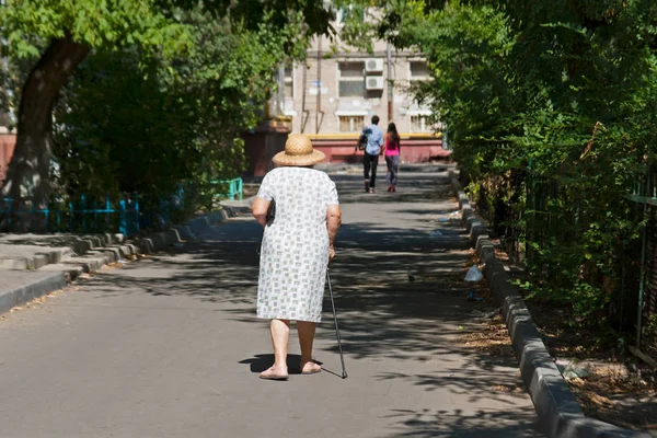 Mujer mayor en sombrero y con un bastón caminando por la calle después de una pareja en verano —  Fotos de Stock