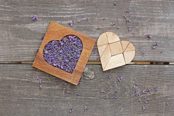 Lavender in wooden heart-shaped box and tangram puzzle in heart shape on wooden background