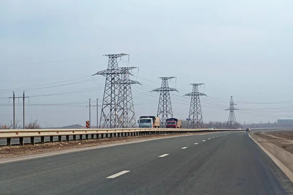 Bilar och lastbilar som kör på motorvägen i bakgrunden av kraftledningar i Volgograd region — Stockfoto