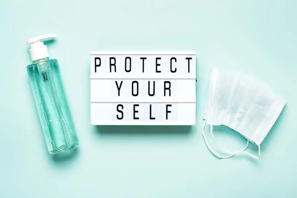 Protective mask and antibacterial gel or soap and PROTECT YOURSELF written on light board. Protecting yourself and others during Coronavirus pandemic. Healthcare, medical and quarantine concept.