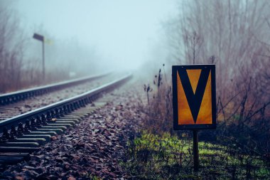Demiryolu tabelası, demiryolu dolgusunda hız limitinin başlaması anlamına geliyor. Demiryolu rayları sisli havada kayboluyor.
