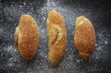 Arkaplanda un ve susam tohumları serpiştirilmiş siyah üzerine susam tohumu serpiştirilmiş üç taze mısır ekmeği yatıyordu.