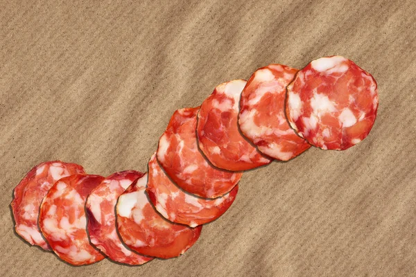 Varkensvlees Salami segmenten op verfrommeld gestreepte Manilla bruin kraftpapier — Stockfoto