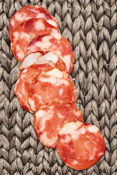 Varkensvlees Salami segmenten op oude Raffia placemat — Stockfoto