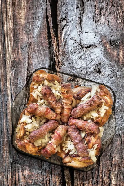 Grilované mleté maso šišky Cevapcici a kuřecí stehna s nakrájenou cibulí v Glass pekáč na staré dřevo — Stock fotografie