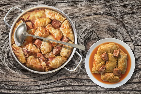 Plateful de rollos de col rellenos con carne picada cocida en salsa de tomate en una olla de acero inoxidable en una mesa de jardín de madera vieja — Foto de Stock