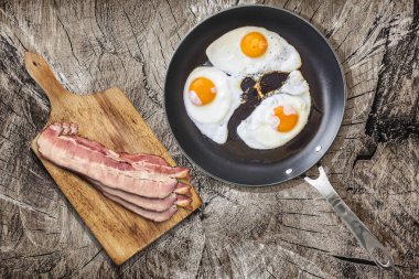 Ağır hizmet Teflon tavada domuz pastırma Rashers üzerinde kesme tahtası ile kızarmış yumurta kadar güneşli tarafı eski kırık ahşap piknik masa ayarla