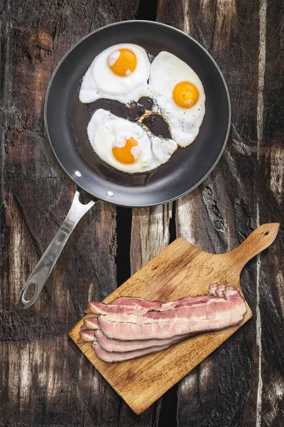 Ağır hizmet Teflon tavada domuz pastırma Rashers üzerinde kesme tahtası ile kızarmış yumurta kadar güneşli tarafı eski kırık ahşap piknik masa ayarla — Stok fotoğraf