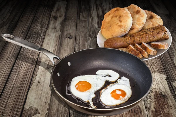 Fried Eggs In Old Teflon Frying Pan With Plateful Of Baguette Slices And Pitta Bread Loafs Set On Old Cracked Flaky Wooden Table — Stock Photo, Image