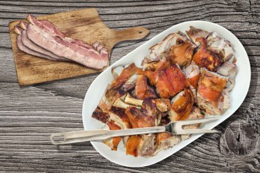 Tabak dolusu tükürük kavrulmuş Pork Omuz dilimleri ve pastırma Rashers kesme tahtası üzerinde eski rustik düğümlü ahşap piknik masa ayarla