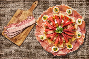 Lezzetli yemek Meze pastırma Rashers ahşap kesme tahtası üzerinde ile kaba Grunge çuval bezi üzerinde ayarla meze zemin Vignetted