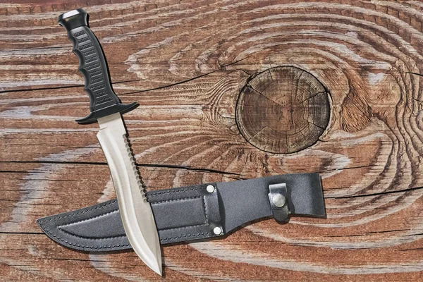 Coltello da caccia tattico di combattimento sopravvivenza Sawback Bowie con guaina in pelle nera incastonata su sfondo in legno di pino rustico annodato vecchio — Foto Stock