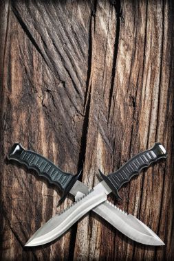 Tactical Combat Hunting Survival Bowie Knives With Crossed Blades On Grunge Vignetted Old Battered Grooved Wood Background clipart