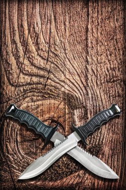 Tactical Combat Hunting Survival Bowie Knives With Crossed Blades On Grunge Vignetted Old Battered Grooved Wood Background clipart