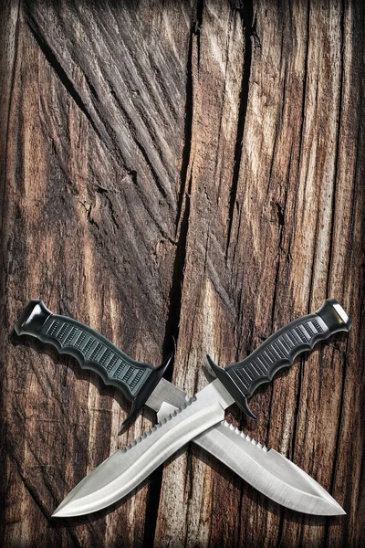 グランジの交差のブレードと戦術的な戦闘の狩猟サバイバル ボウイ ナイフ Vignetted 古いボロボロ溝木材の背景 — ストック写真