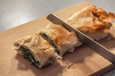 Fırından yeni çıkmış geleneksel Sırp peynir ıspanak pasta rulo ahşap kesme tahtası üzerinde tırtıklı ekmek bıçakla dilimlenmiş