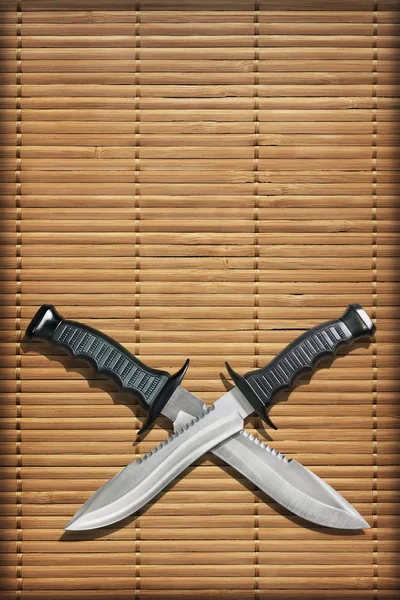 Tático combate caça sobrevivência Bowie facas com lâminas cruzadas em Slatted rústico bambu lugar tapete Vignette fundo — Fotografia de Stock