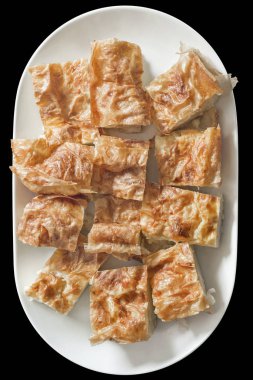 Yüksek çözünürlüklü geleneksel Savory Crumpled Cheese Pie örneği, siyah arka planda izole edilmiş beyaz oblong Porselen tepside sunuluyor..