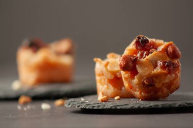 Kuru üzümlü ve fındıklı küçük mini tartlar siyah taşlı yuvarlak tahta üzerinde sade tuşlu..