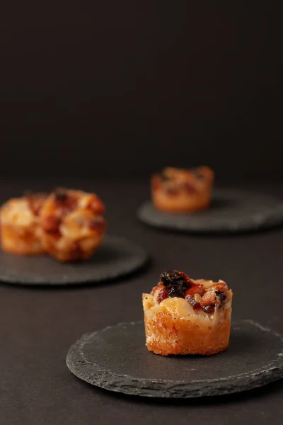 Small mini tarts with raisins and nuts on round black stone board on black in low key.