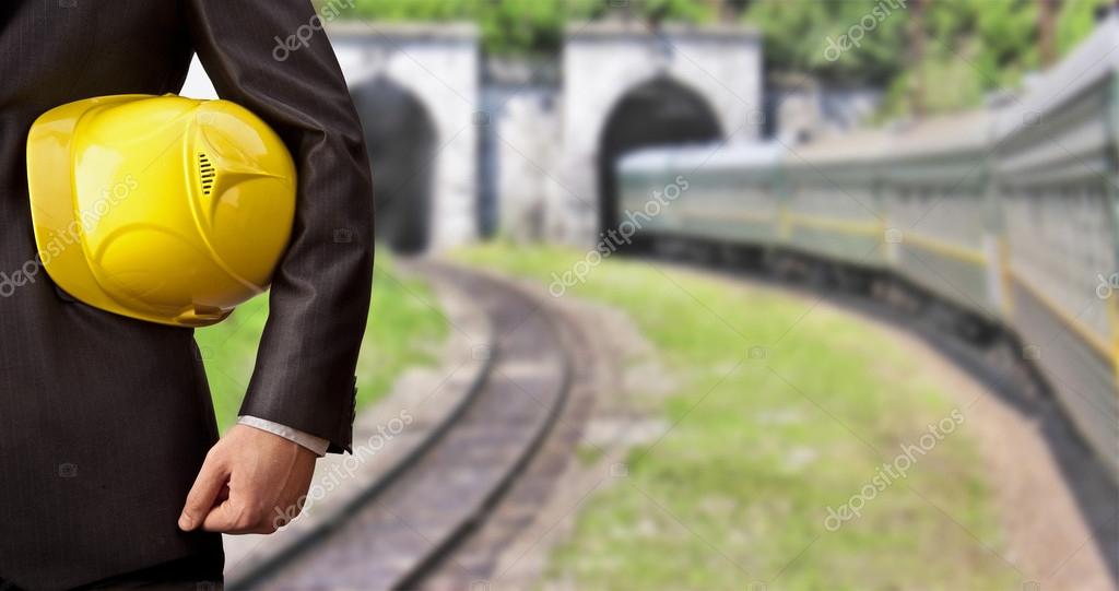 Engineer holding in hand yellow helmet on train and tunnels background. Copy Space for inscription