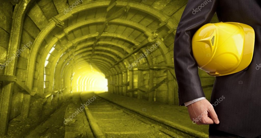 Engineer and worker's  hand holding yellow helmet for workers security against background of an underground mine