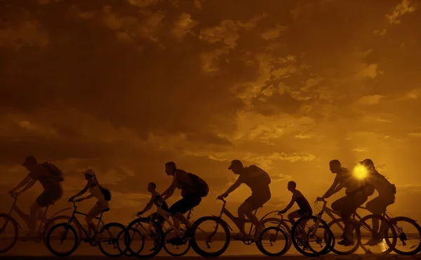 Dark silhouettes of sporty friends on bicycles — Stock Photo, Image